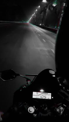 a person riding a motorcycle at night on a street with lights in the dark behind them