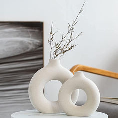 two white vases sitting on top of a table next to a chair and painting