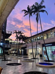 palm trees are in the middle of a shopping mall at dusk, with people walking around