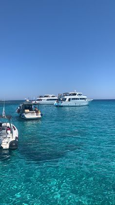 several boats are anchored in the clear blue water on a sunny day with no one around them