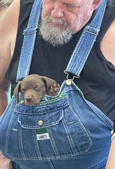 an old man holding a puppy in his back pocket while wearing overalls and looking at the camera