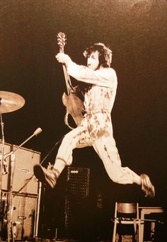 a man jumping up in the air with his guitar and drums behind him on stage