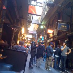 several people are standing in an alleyway with many signs on the buildings and lights above them