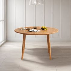 a wooden table sitting in front of a window next to a lamp and some fruit