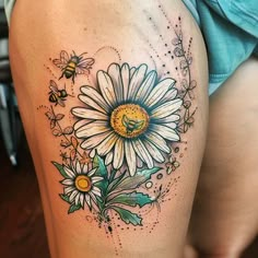 a woman's thigh with a daisy and bees tattoo design on it, while she is wearing a blue shirt