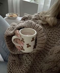 a woman is holding a coffee cup in her hand while sitting on a couch with a blanket over her