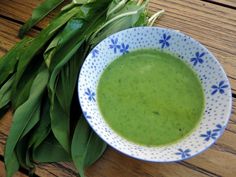 a blue and white bowl filled with green liquid next to some leaves on a wooden table