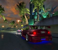 a red car driving down a street next to tall buildings and palm trees at night