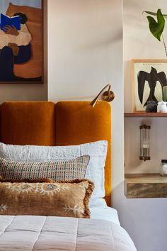 a bed with white sheets and orange headboard next to two pictures on the wall