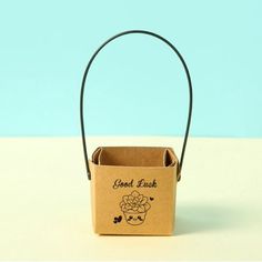 a small brown box with a handle on it that says good luck and has an image of a cupcake in the middle