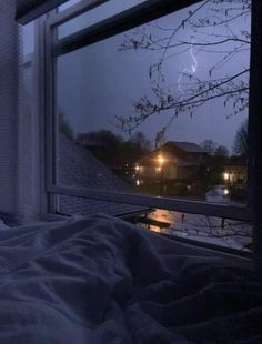 a bedroom with a window that has snow on the ground and trees outside at night