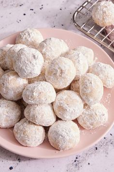 powdered sugar donuts on a pink plate next to a cooling rack and cookie sheet