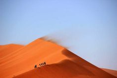 three people walking up the side of a sand dune