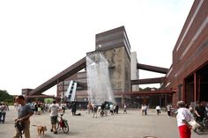 a group of people standing around in front of a building with water spewing out of it