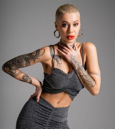 a woman with tattoos on her arms and chest posing for the camera, wearing tight grey clothing