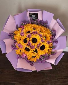 a bouquet of sunflowers and lavender flowers in a purple paper wrapper on a wooden floor