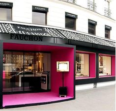 a storefront with pink and black colors on the outside, in front of a tall building