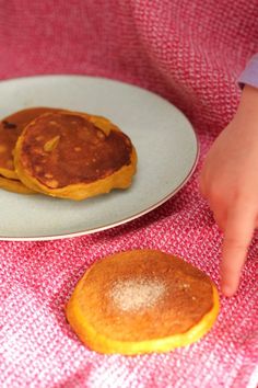 two pancakes on a plate being held by a child's hand and pointing at them