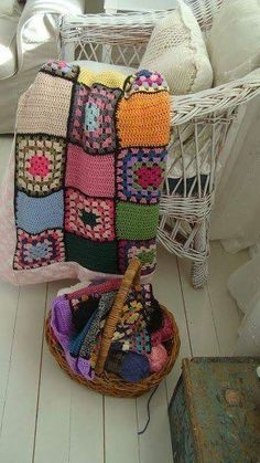 a crocheted blanket sitting on top of a wicker basket next to pillows