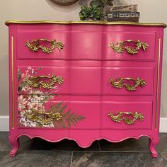 a pink dresser with gold trim and flowers painted on it