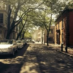 several cars parked on the side of a street next to tall brick buildings and trees