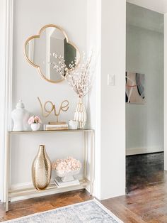 a shelf with vases and flowers on it in front of a mirror, door way to another room