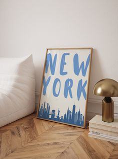 a framed new york poster sitting on top of a wooden floor next to a lamp