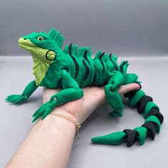 a hand holding a green and black toy lizard