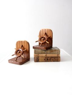 three wooden books stacked on top of each other in front of a white wall and two ships wheel bookends