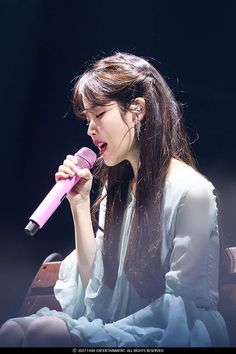 a woman with long hair holding a microphone in her hand while sitting on a chair