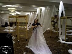 a woman is standing in a room with white sheets on the floor and some people are climbing ladders