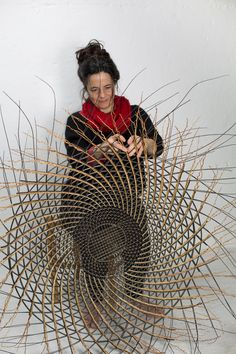 a woman sitting in front of a sculpture made out of sticks and branches with her hands