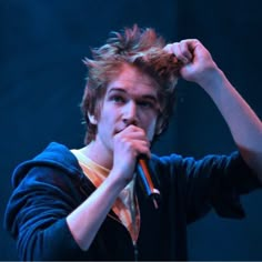 a young man holding a microphone up to his ear while standing in front of a dark background