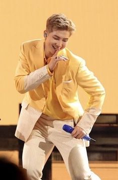 a male in a yellow jacket and white pants is holding a blue object while standing on stage