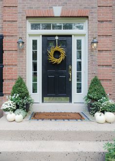 a black front door with two white pumpkins on the steps and a yellow wreath