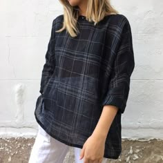 a woman standing in front of a white wall wearing a black and grey plaid shirt