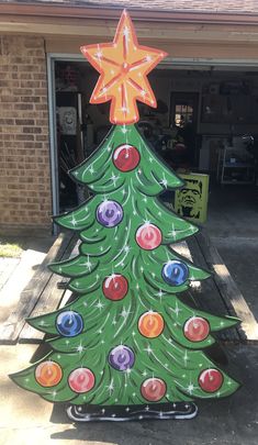 a painted christmas tree sitting in front of a garage