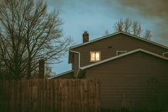 a house with a fence and trees in front of it at night time, looking out the window