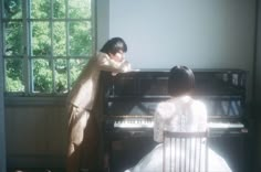 two women standing next to each other in front of a piano and looking at it