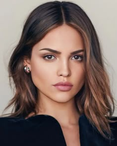 a woman with brown hair and blue eyes wearing a black top is looking at the camera