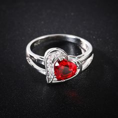 a red heart shaped ring with diamonds on it's sides, sitting on a black surface