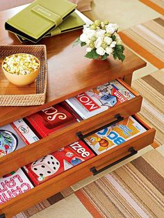 a wooden table topped with two drawers filled with books and magazines next to a bowl of popcorn