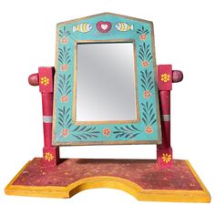 a small wooden mirror sitting on top of a table next to a red and yellow stand