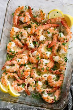 a glass casserole dish filled with shrimp and garnished with lemon wedges