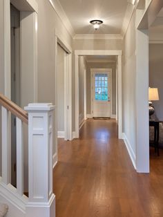 an empty hallway with hard wood floors and white trim on the walls, leading to another room