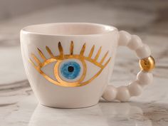 a coffee cup with an evil eye painted on the side and beaded bracelet around it