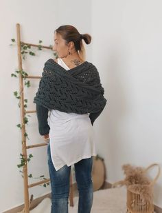 a woman standing in front of a ladder wearing a knitted shawl and jeans