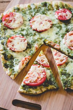 a pizza with tomatoes and spinach is cut into four slices on a cutting board