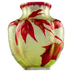 a glass vase with red and green leaves on it's sides, in front of a white background