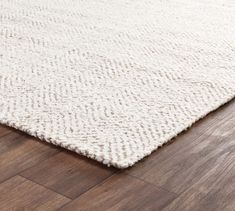 a white rug on the floor with wood floors in the foreground and a brown wooden floor